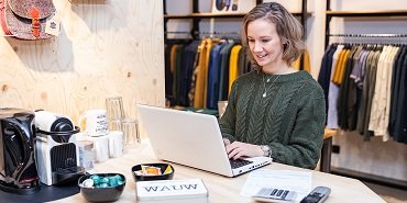 Een ondernemer werkt achter de computer in haar kledingzaak